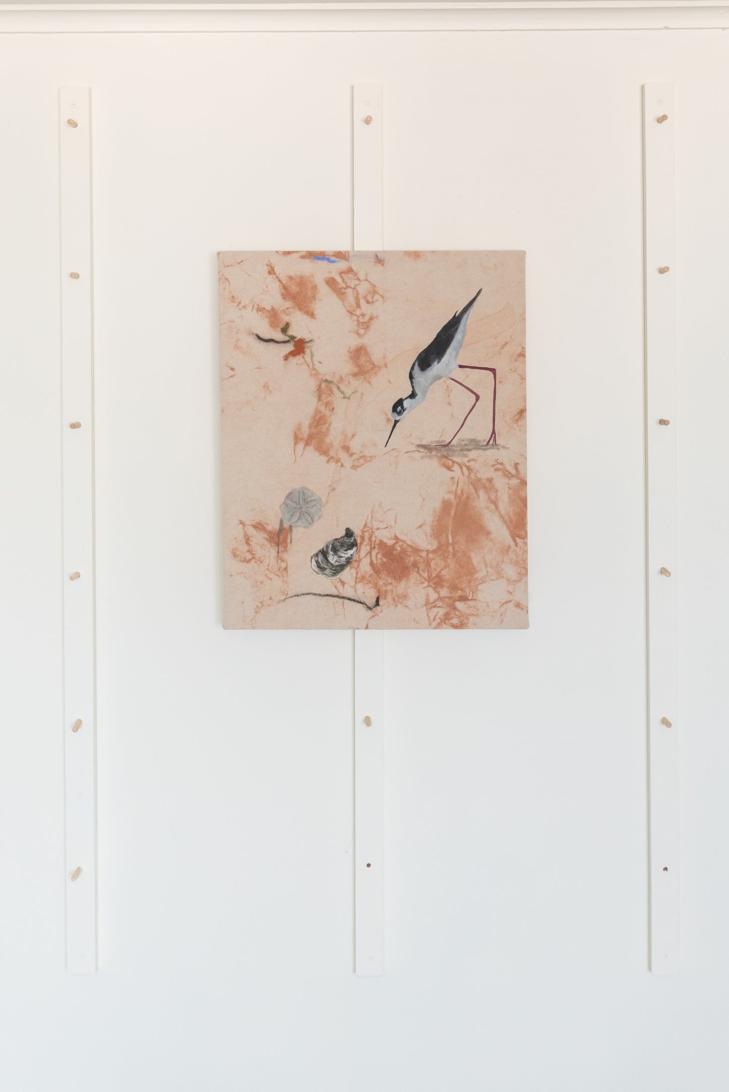Abstract artwork created with PEI red dirt pigments, displayed on a clean white studio wall. The deep earthy reds and browns in the painting stand out against the minimalist background, emphasizing the use of natural materials.
